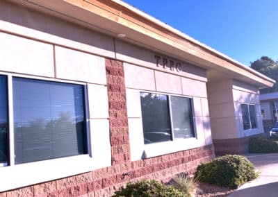 Exterior view of a building with the letters "TPRC" mounted above a row of windows. The structure has a brown and beige color scheme, with shrubs in front. The sky is clear and blue.